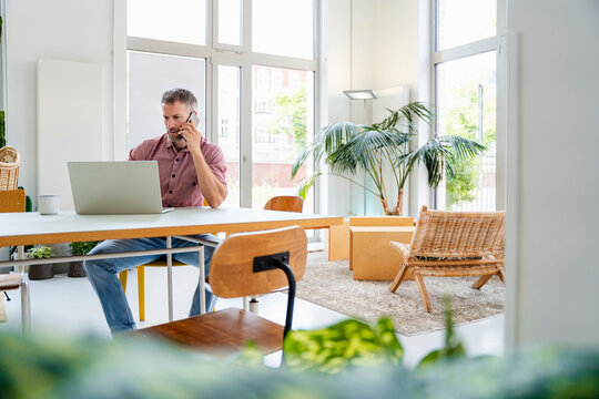 Confident professional using laptop and phone in modern office workspace