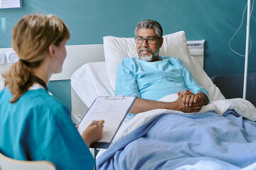 Middle aged biracial man lying in hospital bed interacting with young adult biracial woman...