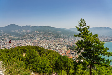 Obraz premium Drone view of Alanya city, Turkey. Coastline, Mediterranean Sea, harbor, historic castle on the hill, and sprawling urban area with mountains in the background on a clear summer day. Alanya, Turkey