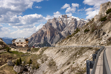 Alpine lodge and winding mountain road at Valparola Pass with dramatic view of Tofana di Rozes in...