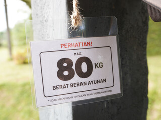 Caution sign displaying maximum weight limit for swing ride and warning against dangerous actions...