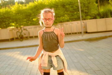 Happy young girl with pink glasses skating in park during golden hour, casual black top and denim...