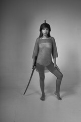 Warrior woman in chainmail and medieval Asian helmet holding traditional Japanese sword katana on...