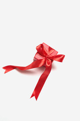 Small red gift box with shiny ribbon sits on a white background, ready for celebration or special...
