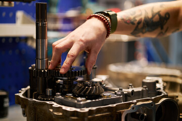 Tattooed mechanic hand repairing gear system in garage workshop