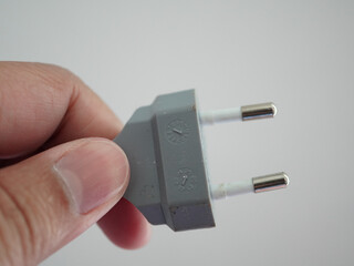 Hand holding a European power plug, ready to connect to an electrical outlet for charging devices