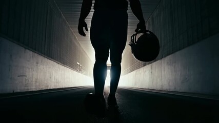 American football player walking through stadium tunnel with helmet in hand, silhouette of athlete entering field from locker room with determination, motivation and mental focus before game - Powered by Adobe