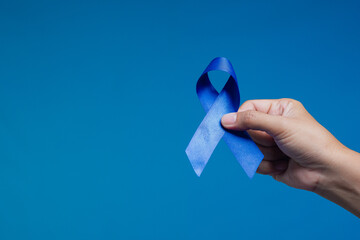 Hand holding blue ribbon symbolizing colon cancer awareness, support, and medical advocacy.