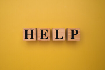 Wooden blocks with word HELP on yellow background symbolizing assistance, support, or urgency.