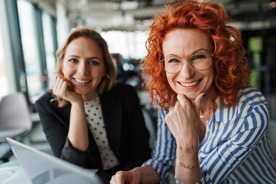 Two female colleagues analyzing project documents in modern office.