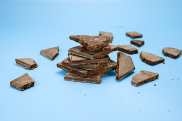 A stack and scattered dark chocolate chuck isolated a blue background. Perfect for advertisements,...