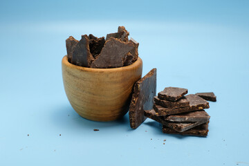 A chunks of dark chocolate inside a small wooden cup, with additional pieces scattered beside it,...