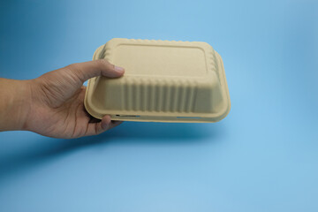 A human hand holding a closed eco friendly food container made of biodegradable material, isolated...