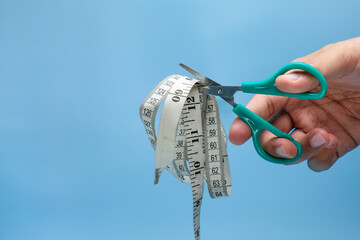 A human hand using a green handled scissor to cut through a measuring tape, set against a blue...