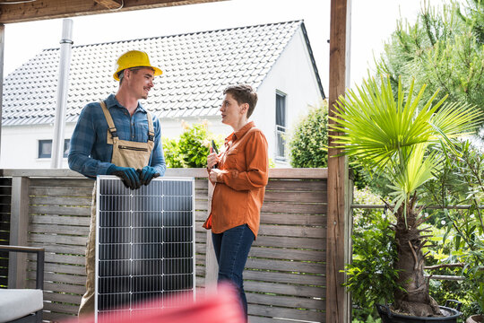 Craftsman giving solar energy advice to woman at home outdoors