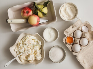 Ingredients for making a curd casserole for breakfast - cottage cheese, apples, sour cream, sugar on a light background, top view
