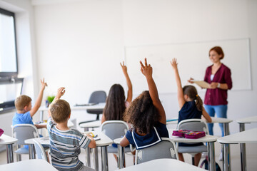 School children sitting at the desk in classroom on the lesson, raising hands.