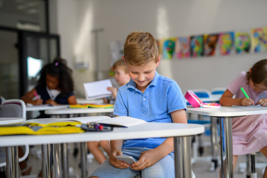 Schoolboy distracted by mobile phone during lesson. - Powered by Adobe