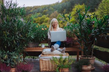 Older woman working from homeoffice, sitting on terrace with laptop.