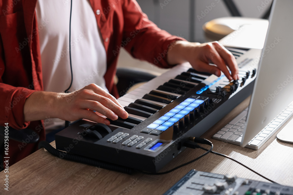 Poster man working with midi keyboard at wooden table indoors, closeup