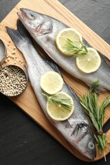 Fresh raw seabass with spices on black table, top view. Fish and seafood delicacies