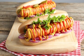 Tasty hot dogs with vegetables, mustard and ketchup on wooden table, closeup