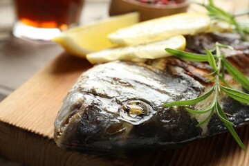 Tasty roasted dorado fish served with rosemary and lemon on wooden table, closeup. Homemade seafood...