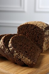 Pieces of fresh rye bread with seeds on wooden board against light grey wall, closeup