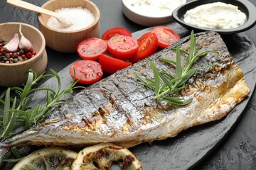 Tasty roasted mackerel served with spices and sauce on black table, closeup. Homemade seafood dish