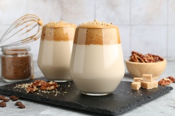 Delicious dalgona coffee in glasses, brown sugar, beans, walnuts, whisk and granules on grey table, closeup