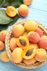 Fresh apricots in wicker basket and green leaves on light blue wooden table, flat lay