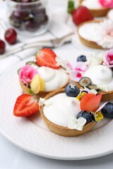 Delicious dessert. Tartlets with cream, berries and flowers on white tiled table, closeup
