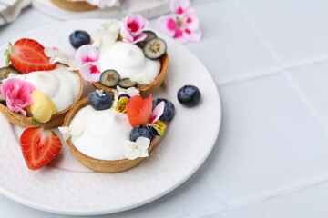 Delicious dessert. Tartlets with cream, berries and flowers on white tiled table, closeup. Space for text