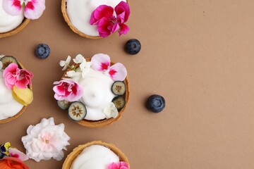 Delicious dessert. Tartlets with cream, berries and flowers on light brown background, flat lay. Space for text