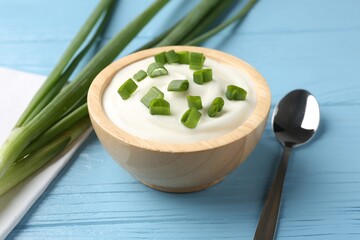 Tasty yoghurt with green onions in bowl on light blue wooden table, closeup