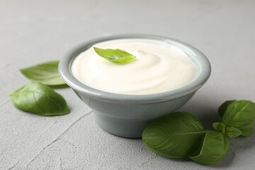 Tasty yoghurt with basil in bowl on light grey table, closeup
