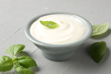 Tasty yoghurt with basil in bowl on light grey table, closeup