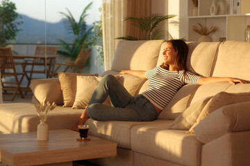Happy woman enjoying her house at sunset on a couch