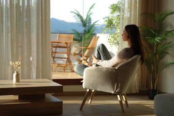 Pensive woman relaxing sitting on armchair in front a window at home