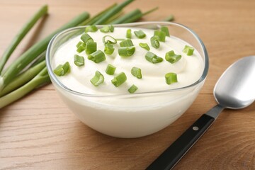 Delicious yogurt in bowl, green onions and spoon on wooden table, closeup