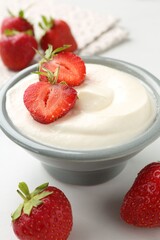 Delicious yogurt in bowl and strawberries on white table, closeup