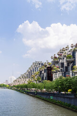 Naklejka premium Shanghai. Innovative buildings adorned with greenery and flowers overlook a lively waterfront in Shanghai's urban landscape.