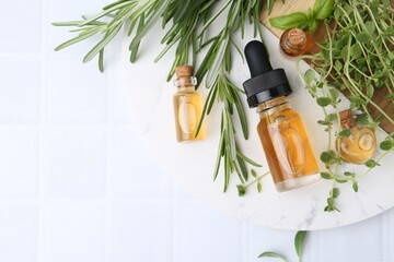 Bottles of essential oil and herbs on white tiled table, flat lay. Space for text