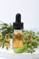Bottles of essential oil and herbs on white table, closeup