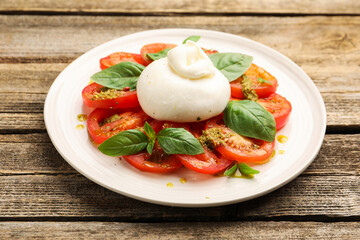 Tasty salad Caprese with mozzarella, tomatoes, basil and pesto sauce on wooden table, closeup