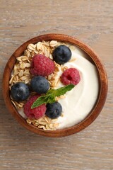 Tasty yogurt with granola and berries in bowl on wooden table, top view