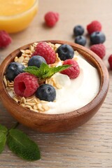 Tasty yogurt with granola, honey and berries in bowl on wooden table, closeup
