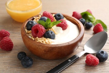 Tasty yogurt with granola, honey and berries in bowl on wooden table, closeup