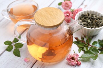 Tasty rose tea, flowers and leaves on white wooden table, closeup