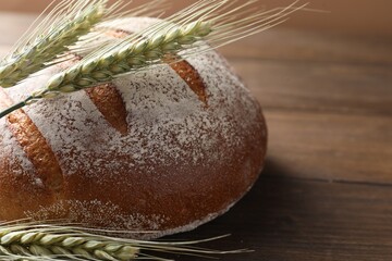 Fresh bread and green wheat spikes on wooden table, closeup. Space for text